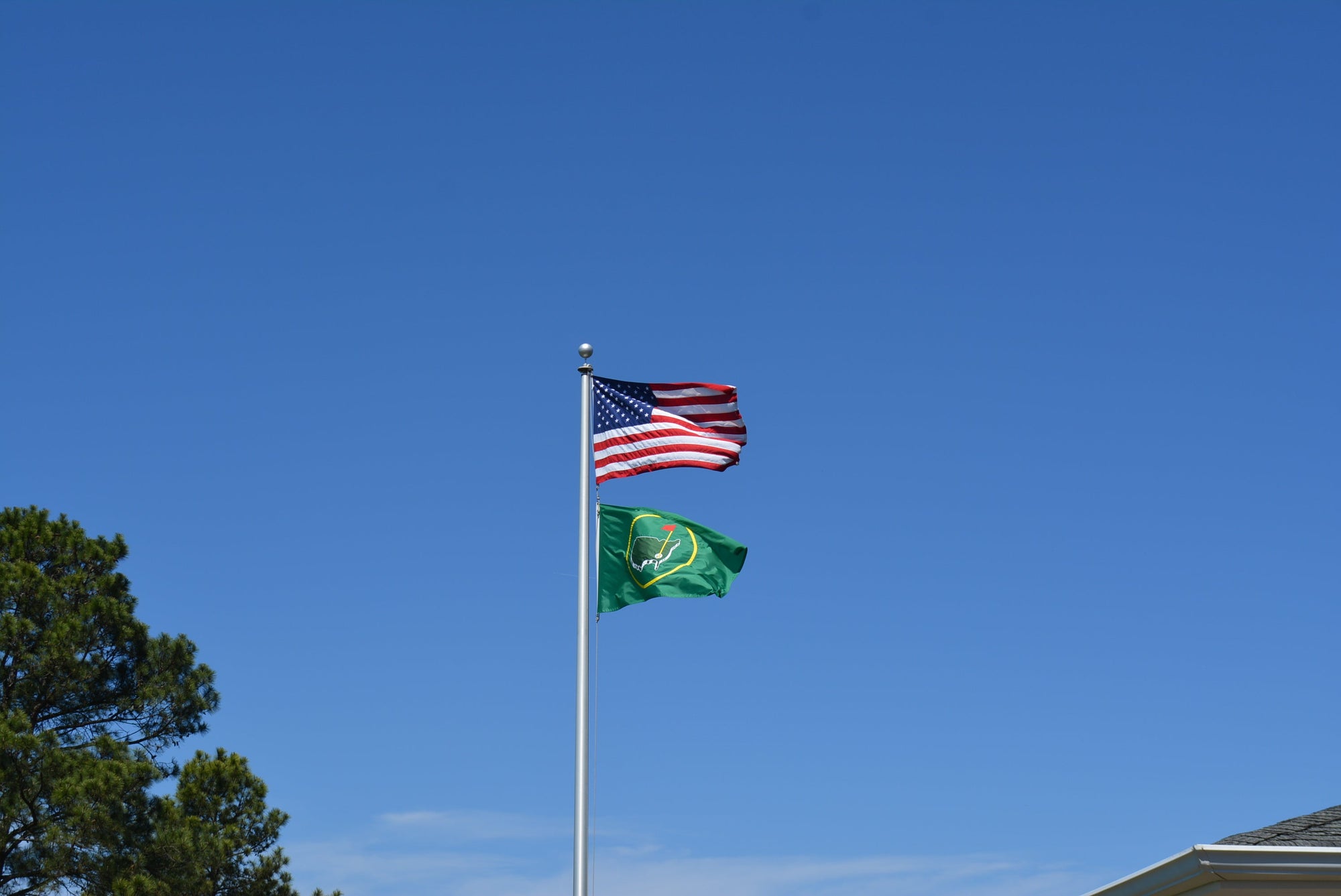 American flag and a green flag with a golf emblem flying on one pole against a clear blue sky.