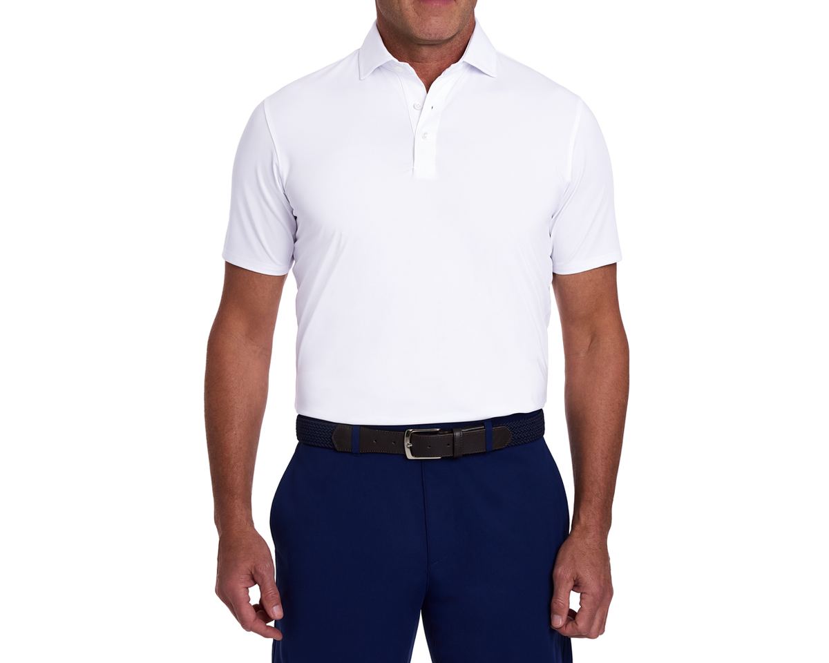The Anderson Shirt: White polo with short sleeves, tucked into navy trousers, featuring a black braided belt. Offers stretch, moisture wicking, and soft jersey knit fabric.