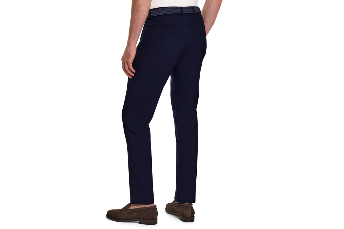 The McDaniel 5 Pocket Pant: Navy, slim-fit, shown from the back with woven belt and brown suede loafers, highlighting wrinkle-resistant, eco-friendly stretch fabric for versatile wear.