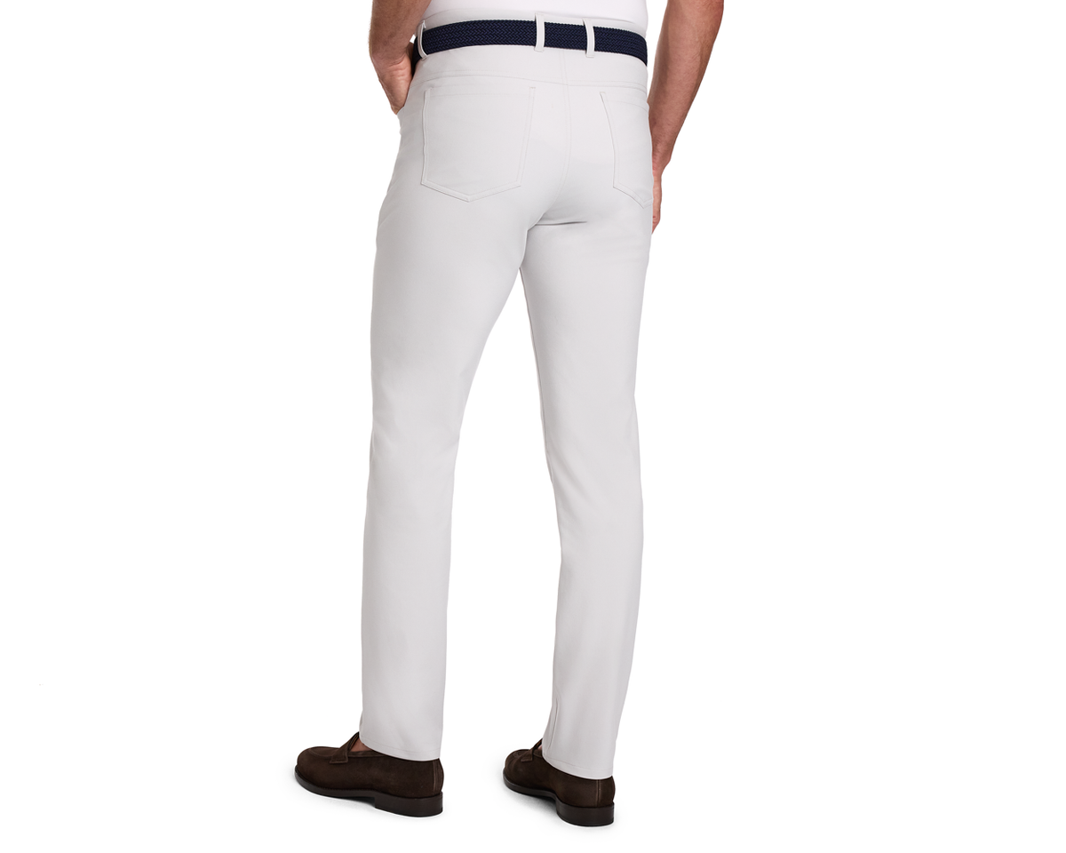 The McDaniel 5 Pocket Pant: Stone, shown from the back, features a slim fit, navy belt, and brown loafers, highlighting its versatile, wrinkle-resistant design.