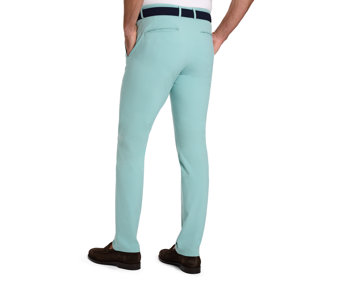 The Anson Chino Pant: Cascade Green, shown with welt back pockets and a navy belt, offers a slim fit, wrinkle resistance, and eco-friendly stretch fabric.