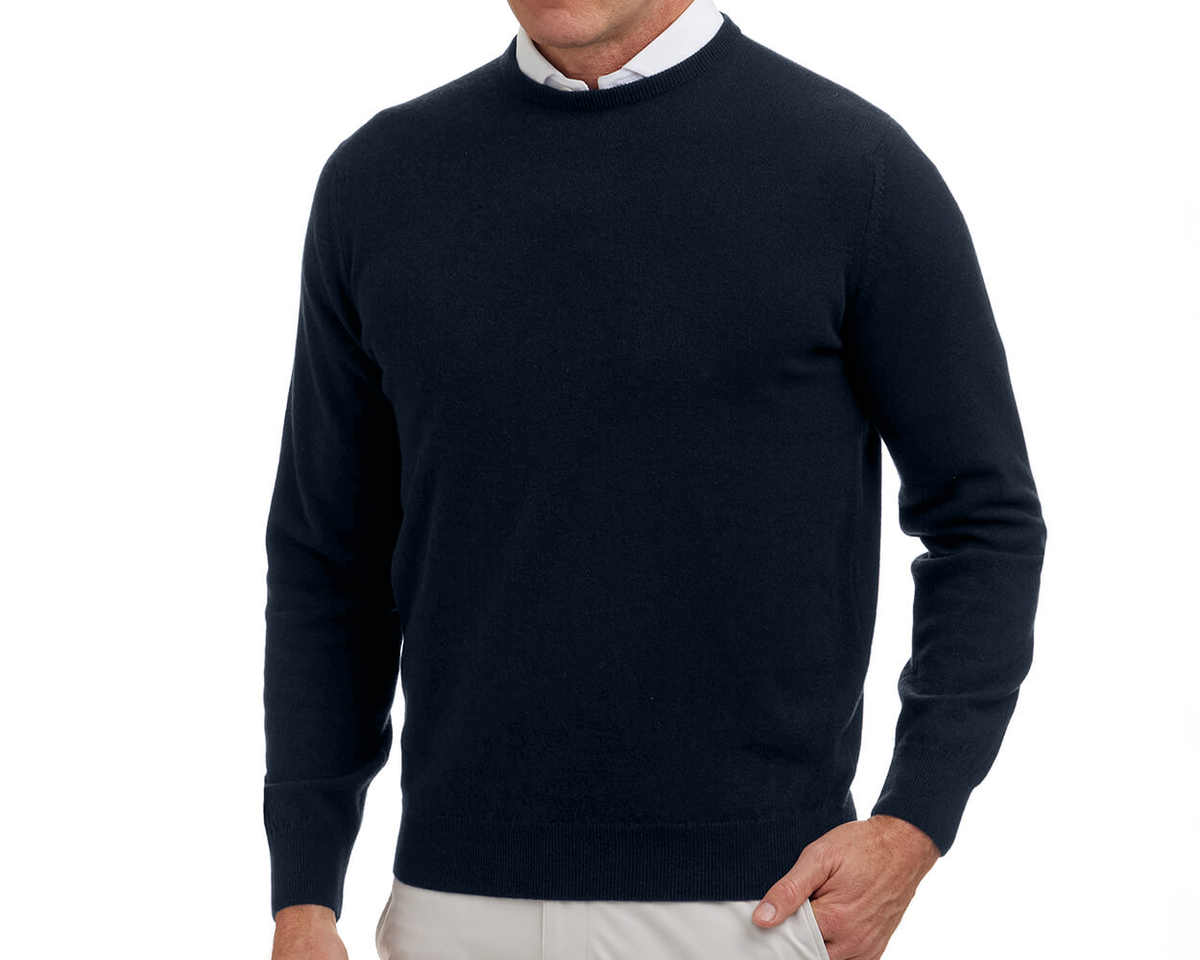 The Buckley Crewneck Sweater in heathered dark navy, layered over a white shirt, showcases Scottish cashmere's quality with a doubled cuff, styled with light trousers.