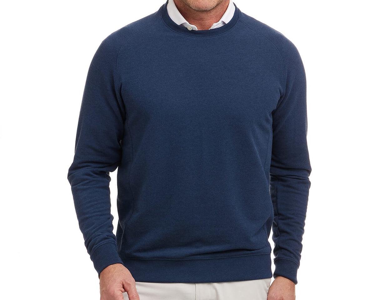 Man wearing The Kennedy Crewneck: Heathered Atlantic, a navy-blue sweatshirt over a white collared shirt. Offers comfort with its plush terry interior.