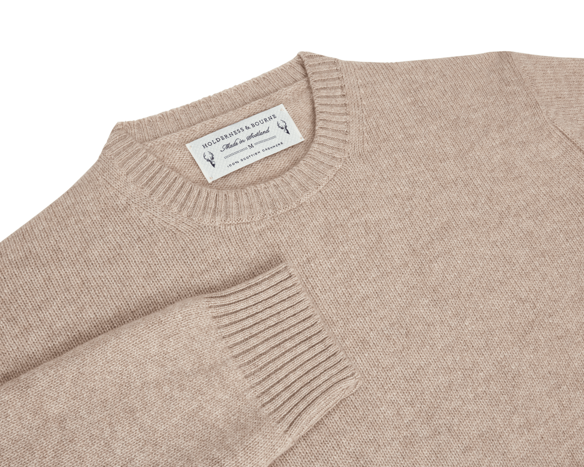 The Berwick Crewneck Sweater: Heathered Dune, in beige Scottish cashmere, features a folded sleeve, sewn-in label, and reinforced cuffs, showcasing premium craftsmanship.