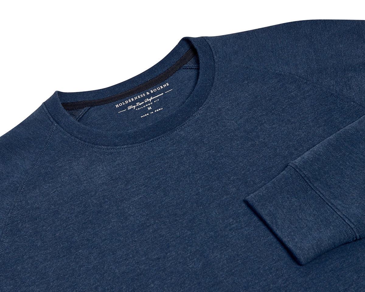 The Kennedy Crewneck: Heathered Atlantic, a navy-blue sweatshirt with a ribbed cuff, showcasing a tailored fit and performance design with a plush terry interior.