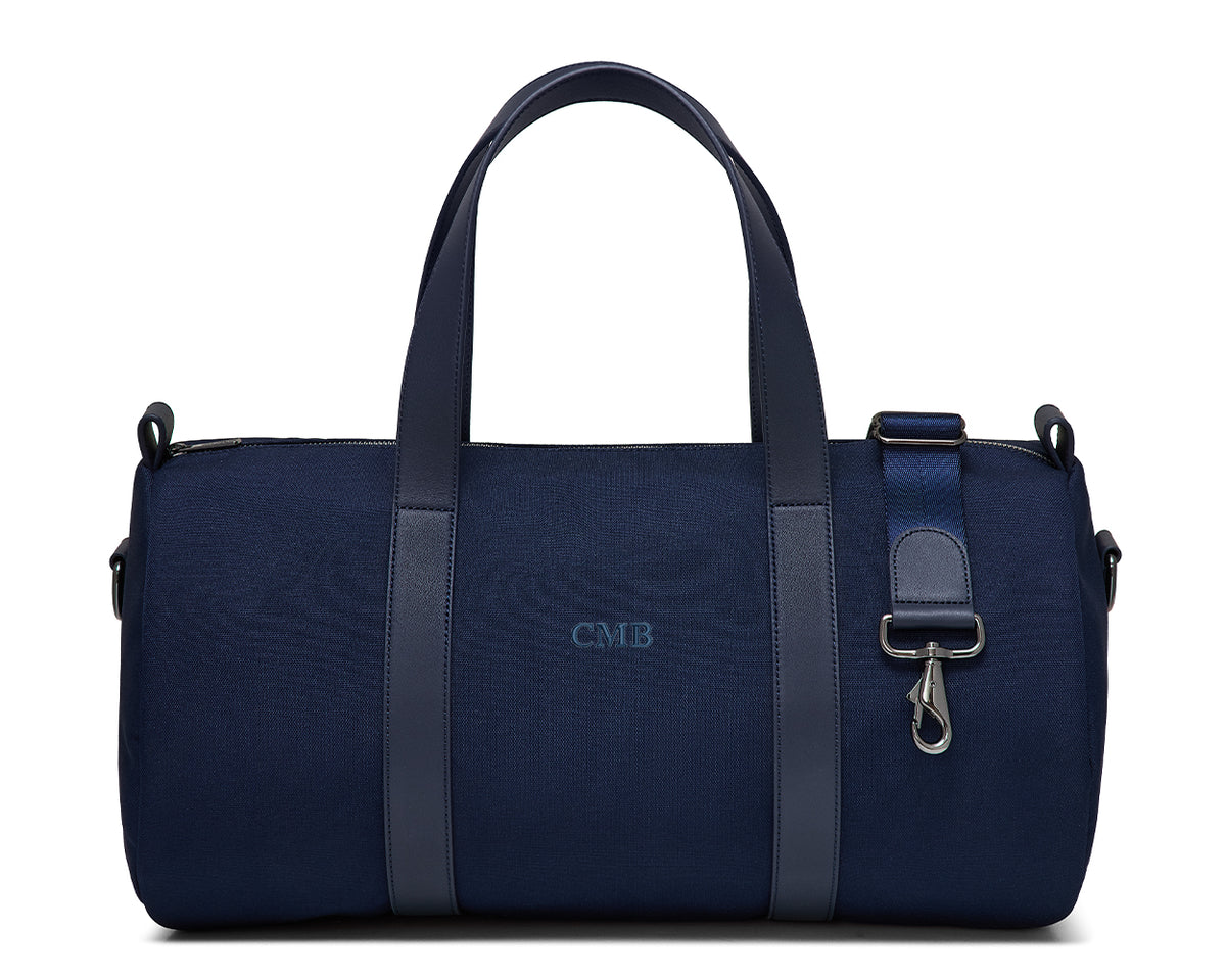 The Marston Banker Bag: Navy Ballistic - Navy Embroidery, features a cylindrical design, two handles, adjustable strap, and CMB monogram, ideal for gym or club outings.