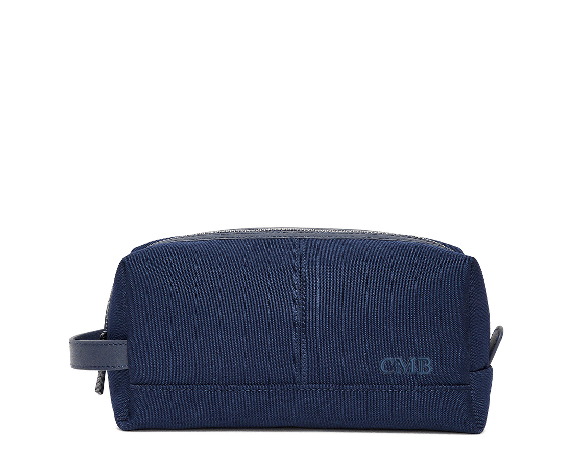 The Littler Dopp Kit: Navy Ballistic - Navy Embroidery, a sleek navy travel toiletry bag with a leather handle, top zipper, and debossed CMB initials.