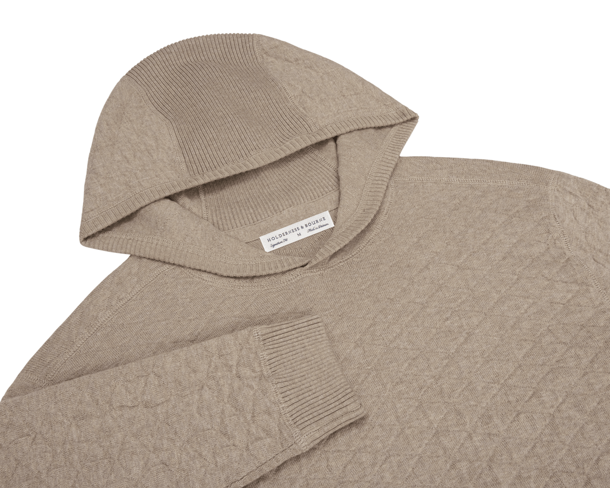 The Wallace Hoodie Sweater: Heathered Light Dune features a ribbed hood, diamond-knit texture, and ribbed cuffs, crafted from 100% Egyptian cotton for warmth.
