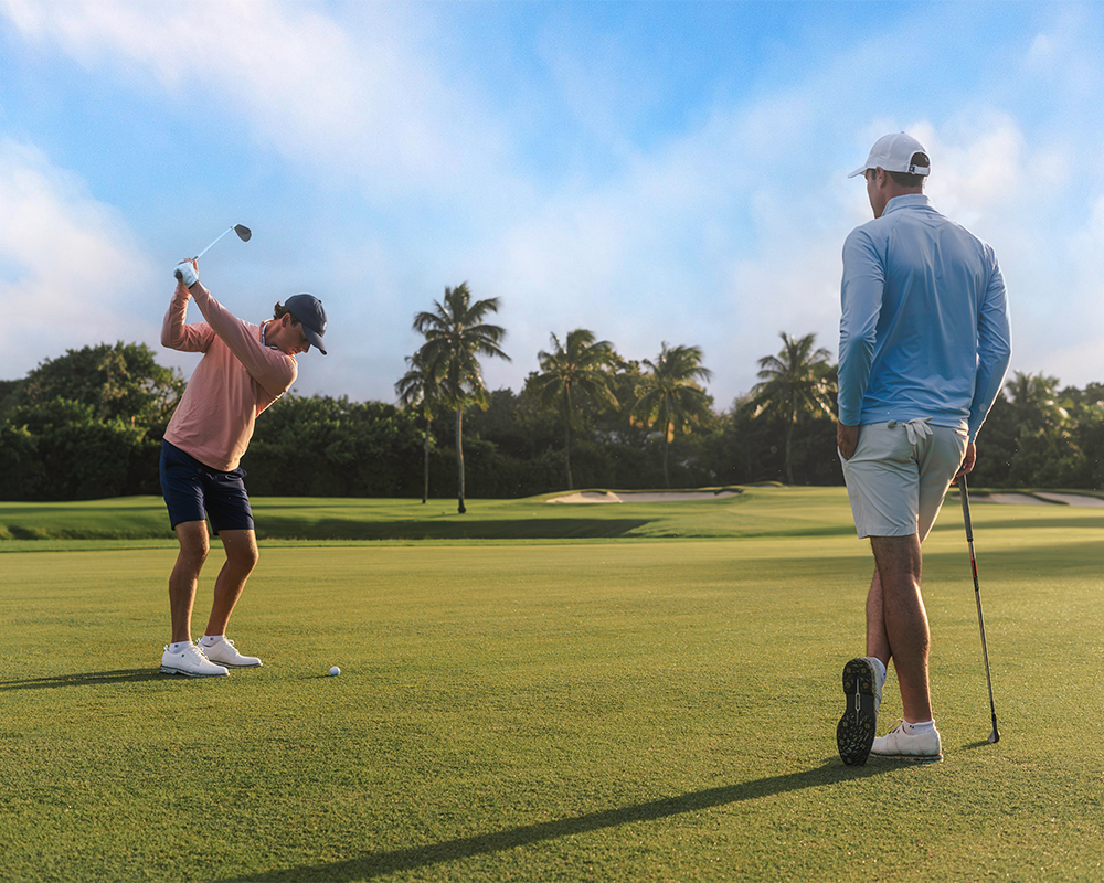 Two men playing golf on a sunny day with palm trees in the background