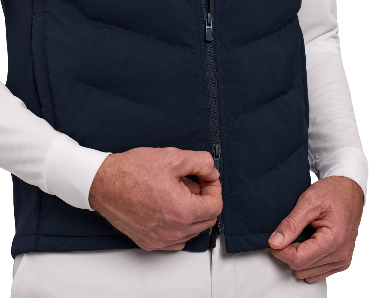 Hands fastening The Benton Vest's two-way zipper, showcasing its quilted front and comfortable knit back for mobility and warmth.
