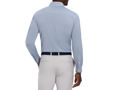 Back view of a male model wearing The Goodrich Shirt: Pacific Blue, showing the yoke, buttoned cuffs, navy woven belt, and light gray pants.