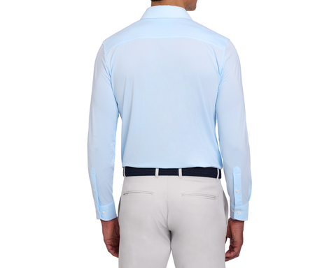 Back view of a male model wearing The Goodrich Shirt: Vista Blue, showing the yoke, buttoned cuffs, navy woven belt, and light gray pants.