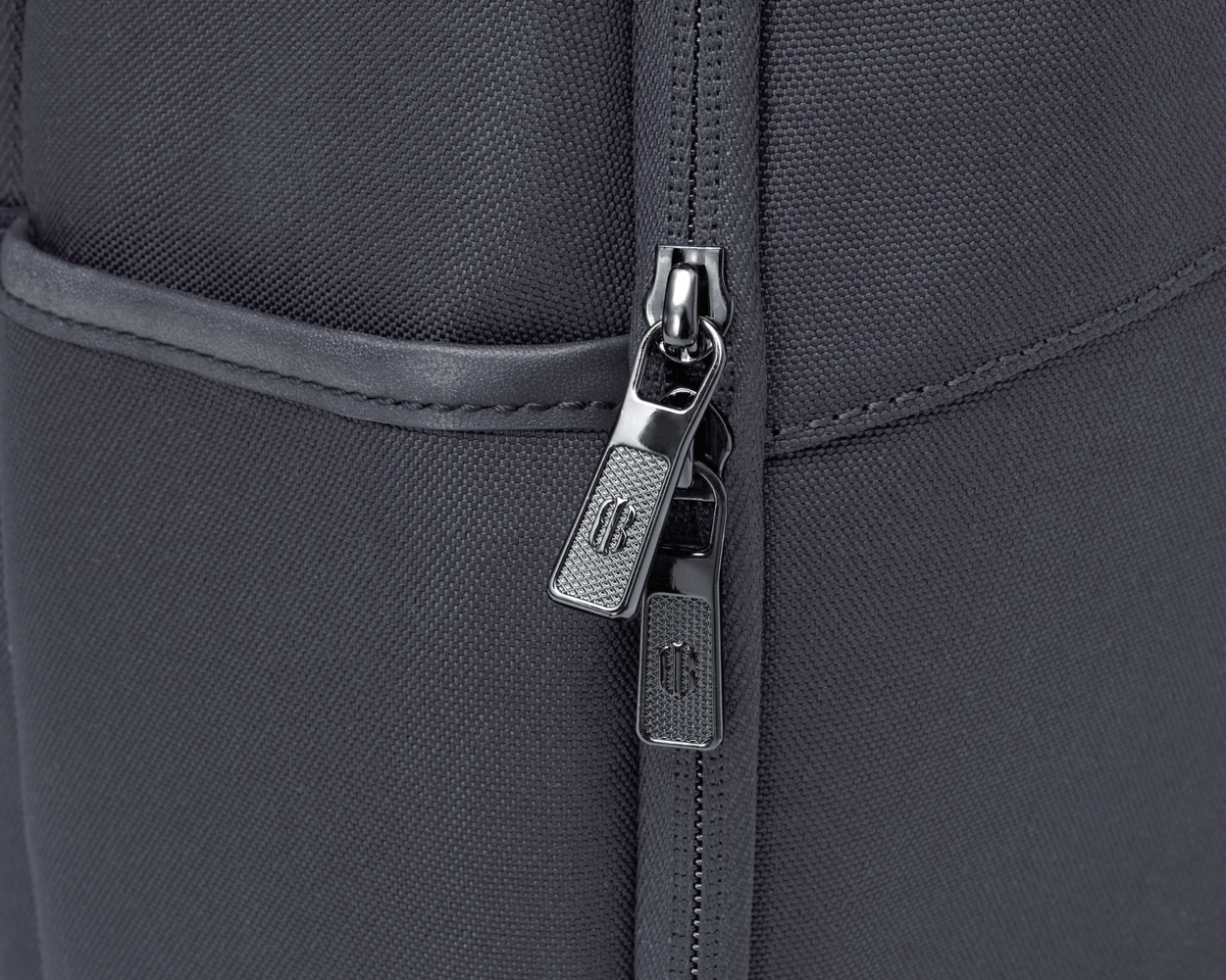Close-up of The Broughton Backpack: Dark Gray showing the woven ballistic nylon, gunmetal zipper pulls, and leather-trimmed pocket edge.
