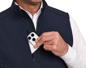 Person placing a smartphone into the zippered chest pocket of The Boyd Vest: Navy, highlighting its windproof and water-resistant features with four-way stretch for ease.