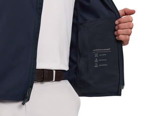The Boyd Vest: Navy, unzipped to reveal an inside pocket, showcases its 4-way stretch, wind-resistant, and water-resistant features, worn over a white polo.