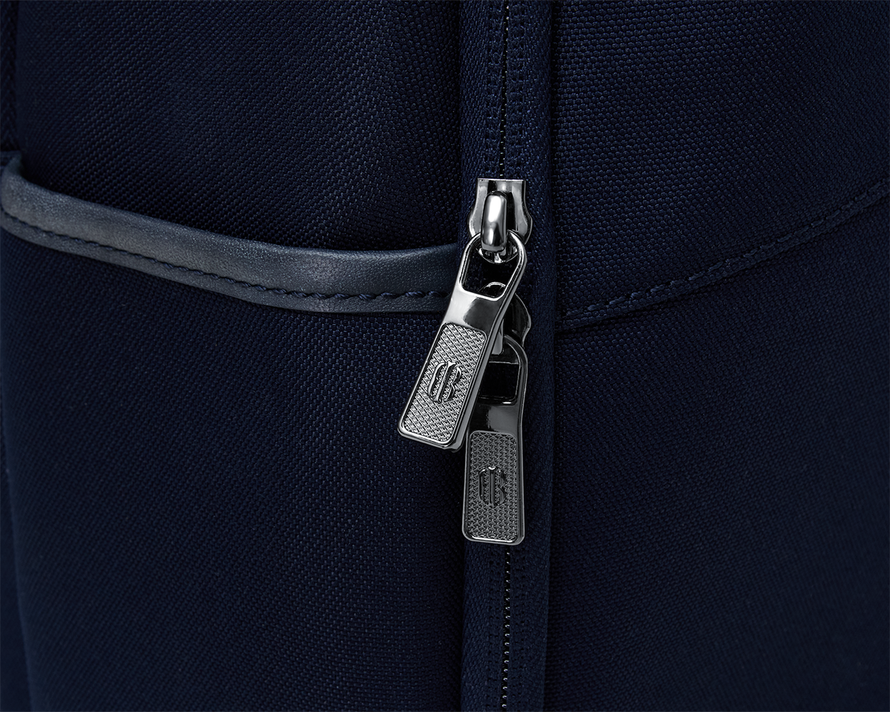 Close-up of The Broughton Backpack's silver zipper pulls on navy fabric, highlighting its durable, stylish design with leather and gunmetal chrome trim.