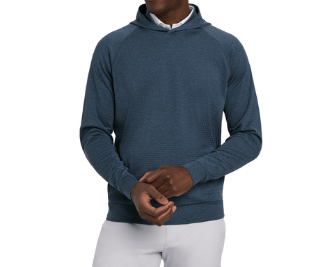 Model wearing The Ellison Hoodie: Heathered Pacific Blue with hands clasped, showing the banded hem, white collar, and light gray pants.
