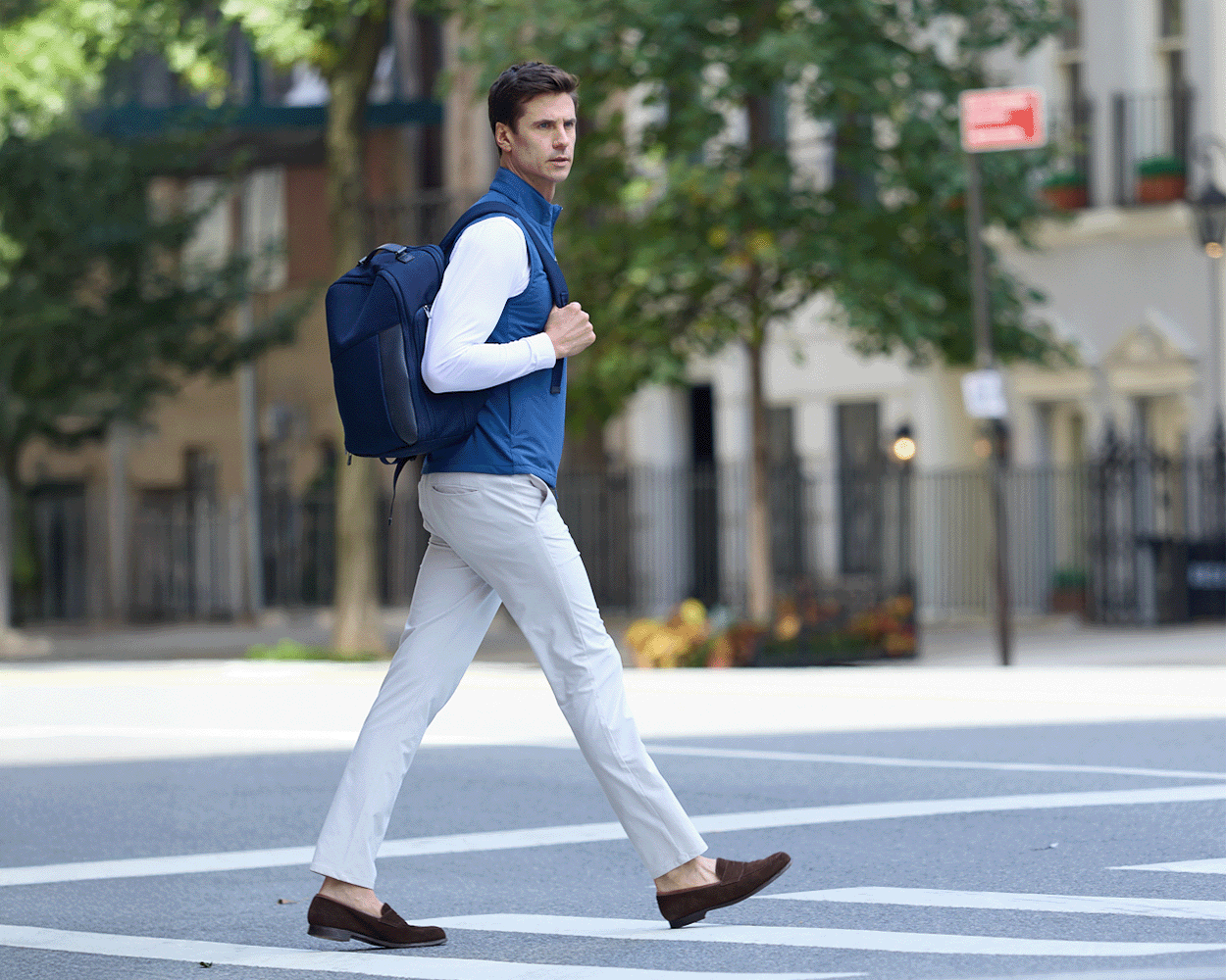 Man wearing The Broughton Backpack: Navy Ballistic - Navy Embroidery, smart-casual outfit, walking in urban street, showcasing the backpack's stylish, durable design.
