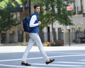 Man wearing The Broughton Backpack: Navy Ballistic - Navy Embroidery, smart-casual outfit, walking in urban street, showcasing the backpack's stylish, durable design.