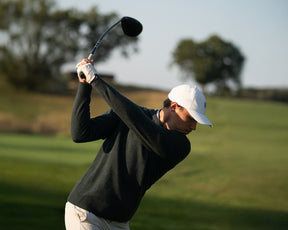 Golfer wearing The Logan Hoodie Sweater in mid-swing, showcasing its minimalist design and luxurious Merino wool-cashmere blend for comfort and versatility.