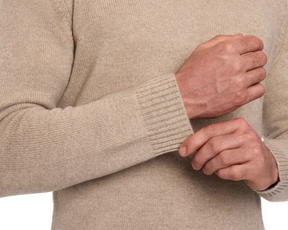 The Berwick Crewneck Sweater: Heathered Dune, showcasing its rib-knit texture and reinforced cuffs as hands adjust the sleeve for a classic fit.