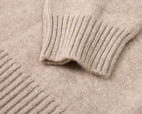 The Berwick Crewneck Sweater: Heathered Dune, showcasing a ribbed cuff and smooth stockinette-knit body, highlighting its plush, three-ply Scottish cashmere craftsmanship.