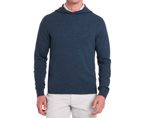 The Logan Hoodie Sweater: Heathered Andover, a navy-blue knit pullover with a hood, worn over a white shirt and paired with beige trousers.