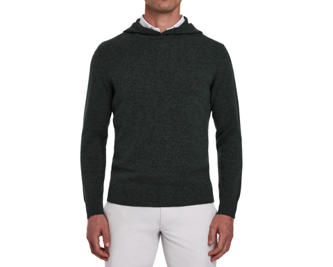 Man wearing The Logan Hoodie Sweater: Heathered Ivy, a knit hoodie over a white shirt, paired with light-gray pants, showcasing its minimalist design and ribbed details.