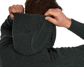 Person lifting the hood of The Logan Hoodie Sweater: Heathered Ivy, showcasing its rib-knit texture, crafted from a soft Merino wool and cashmere blend.