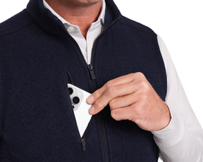 A person uses a white smartphone with The Ashby Vest: Heathered Dark Navy, showcasing its zippered chest pocket and comfortable, stylish design.