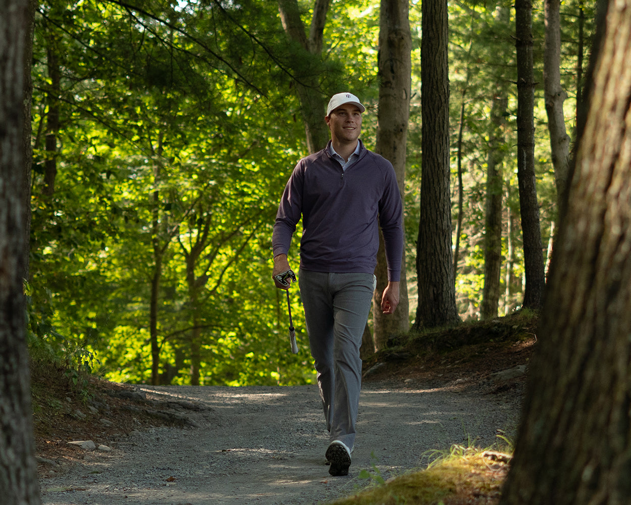 A man strolls on a forest path wearing The Westland Quarter-Zip: Heathered Amherst, showcasing its soft, moisture-wicking fabric and versatile golf-ready design.