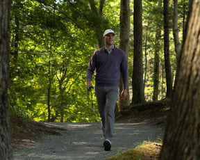 A man strolls on a forest path wearing The Westland Quarter-Zip: Heathered Amherst, showcasing its soft, moisture-wicking fabric and versatile golf-ready design.