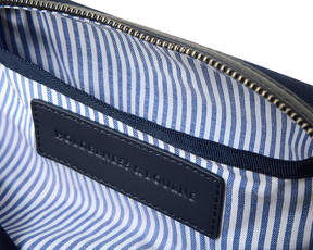 Interior of The Littler Dopp Kit: Navy Ballistic - Navy Embroidery, showcasing a brass-tone zipper, blue-and-white pin-stripe lining, and navy leather brand label.