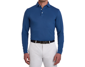 The Abbott Shirt: Andover, a long-sleeve polo in blue, worn with gray trousers. Features a spread collar, contrast piping, and breathable performance fabric.