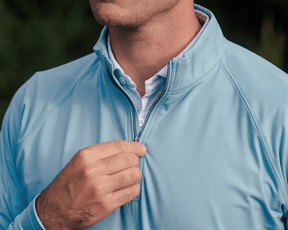 Man adjusting the zipper on The Westland Quarter-Zip: Heathered Harbor, showcasing its lightweight, soft feel and stylish versatility for on and off the course.