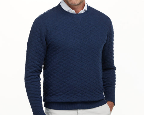 The Ward Crewneck Sweater: Heathered Navy, featuring a diamond-quilted pattern, layered over a white shirt, with the man's hand in trouser pocket.