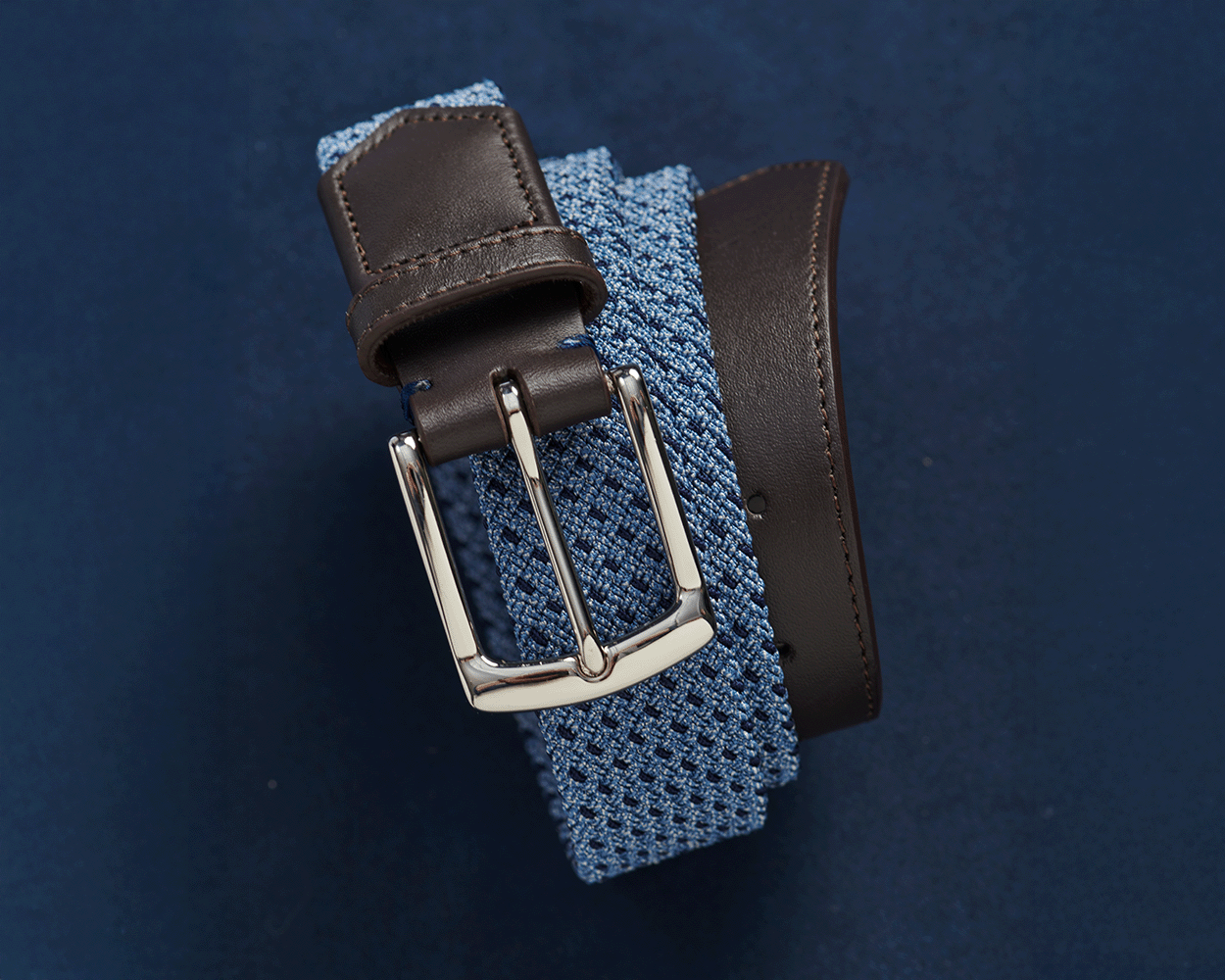 The Fischer Belt: Slate & Navy Basketweave features a light-blue woven strap, dark brown leather trim, and a polished silver buckle.
