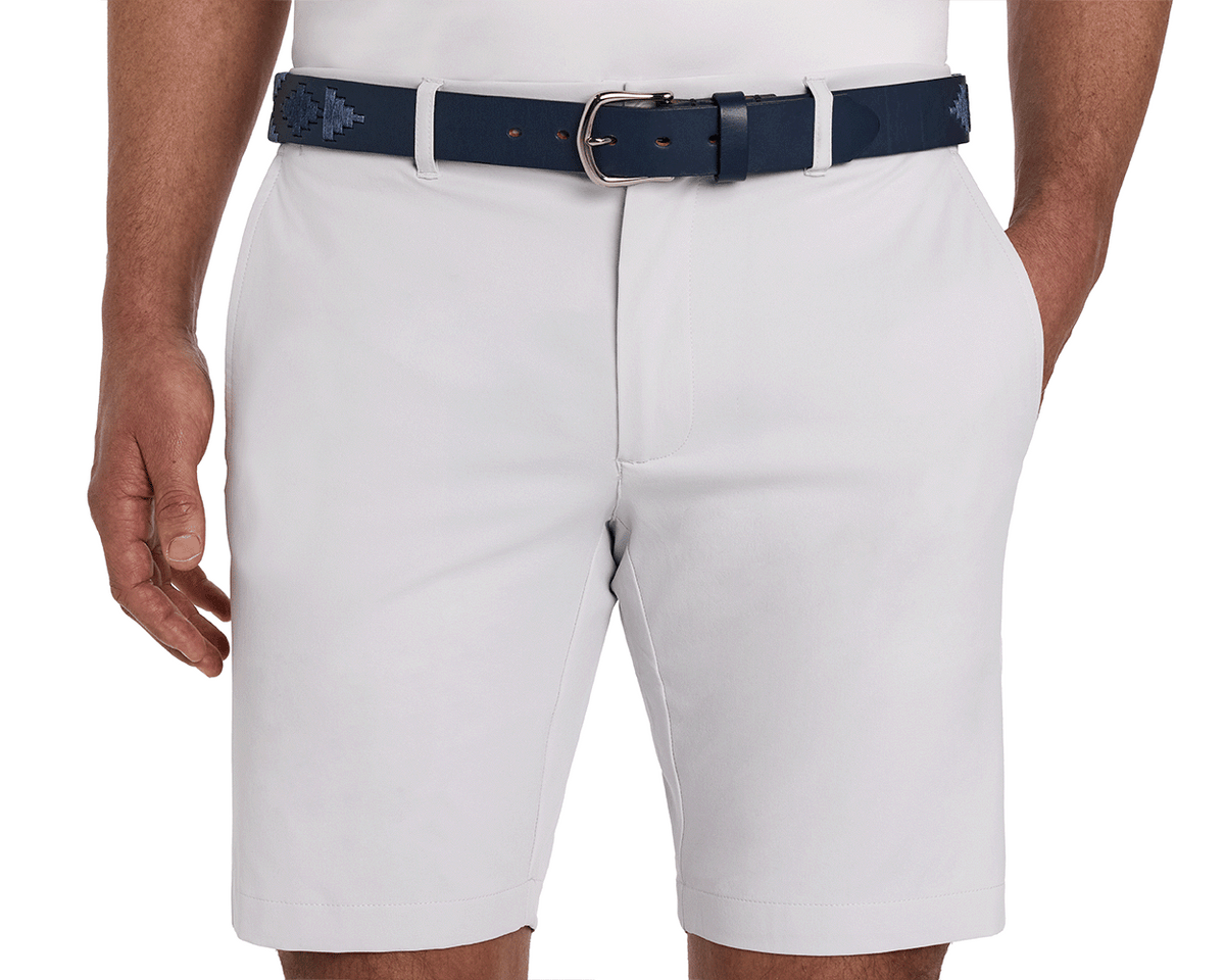 The Barker Belt: Navy & Slate, featuring intricate Argentinean-inspired patterns, is shown threaded through light-gray shorts, paired with a tucked-in white shirt.