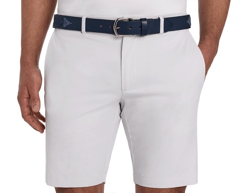 The Barker Belt: Navy & Slate, featuring intricate Argentinean-inspired patterns, is shown threaded through light-gray shorts, paired with a tucked-in white shirt.