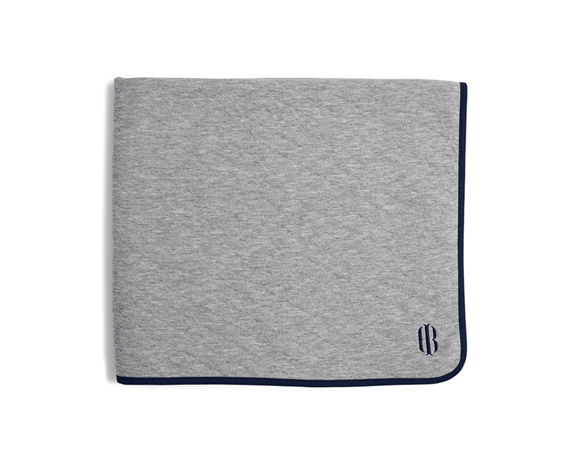The Van Pelt Blanket: Heathered Gray with navy trim and embroidered logo, folded, showcasing its cozy, quilted fabric ideal for warmth and style.
