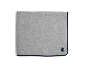 The Van Pelt Blanket: Heathered Gray with navy trim and embroidered logo, folded, showcasing its cozy, quilted fabric ideal for warmth and style.