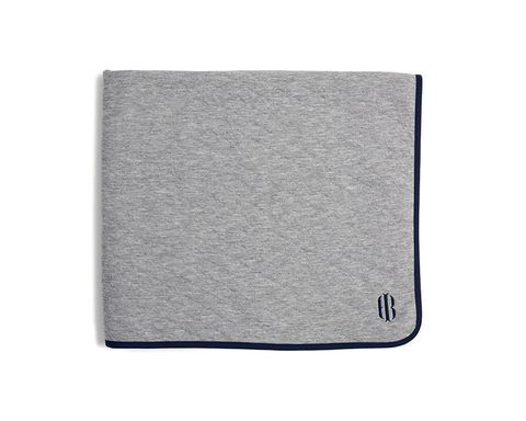 The Van Pelt Blanket: Heathered Gray with navy trim and embroidered logo, folded, showcasing its cozy, quilted fabric ideal for warmth and style.