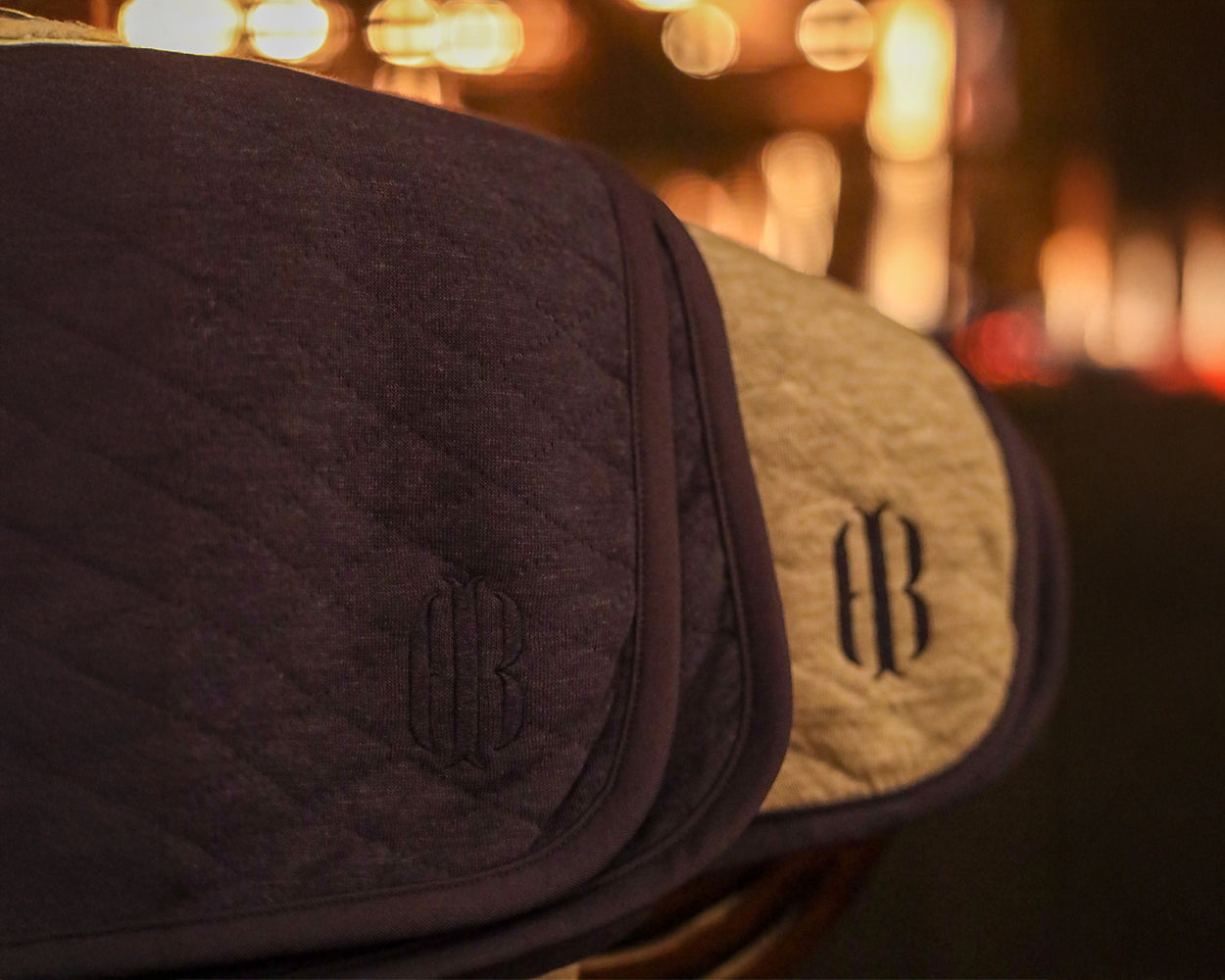 The Van Pelt Blanket: Heathered Navy, quilted fabric with embroidered logo, hangs beside a beige one, showcasing its cozy, elegant design.