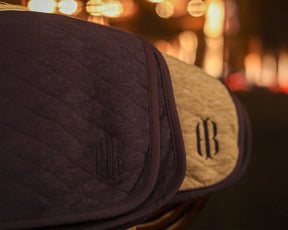The Van Pelt Blanket: Heathered Navy, quilted fabric with embroidered logo, hangs beside a beige one, showcasing its cozy, elegant design.