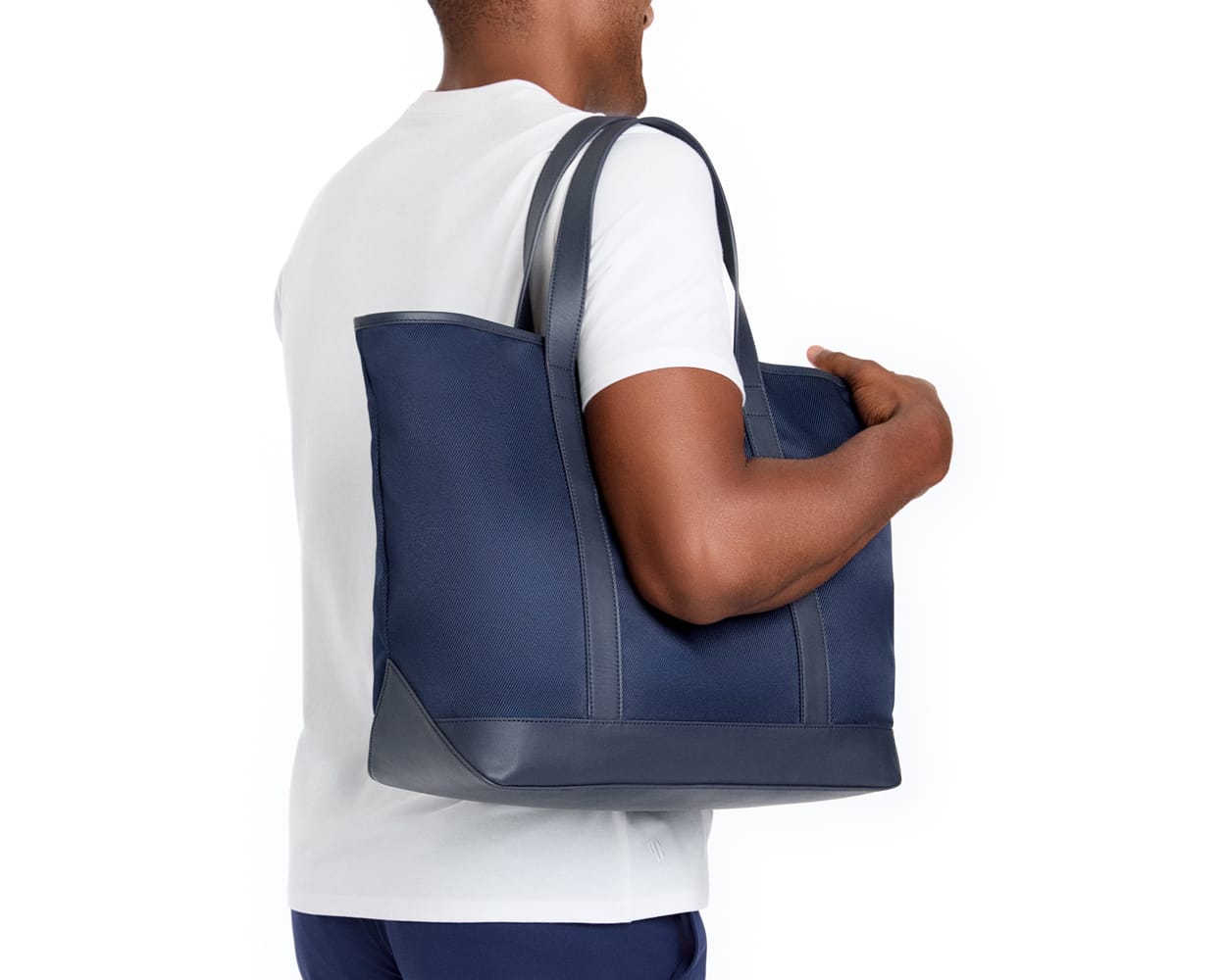 The Treadwell Tote: Navy Ballistic -White Embroidery, features a sturdy navy tote with leather trim, carried on a shoulder, showcasing its durable design.