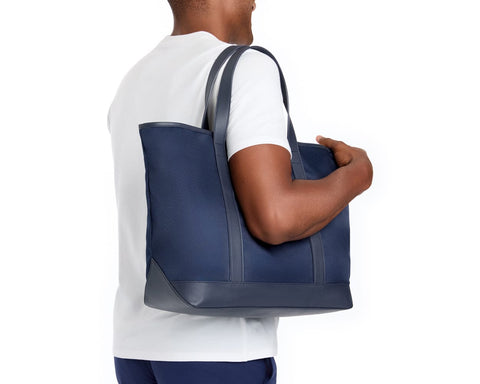 Person carrying The Treadwell Tote: Navy Ballistic with leather trim, featuring a durable fabric and interior pocket, ideal for various occasions.