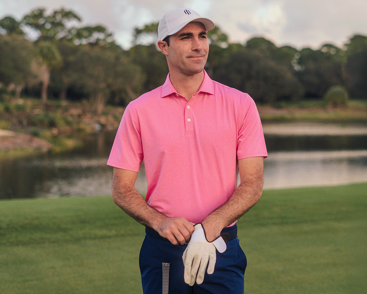 Man on golf course wearing The Holland Shirt: Heathered Belmont, a polo with heathered stripes, as he holds a golf club and adjusts his glove.