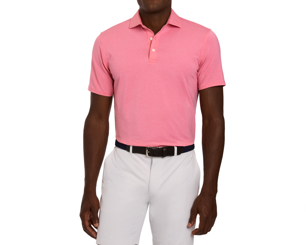 Person wearing The Holland Shirt: Heathered Belmont, a short-sleeve pink polo with subtle stripes and structured collar, tucked into light gray trousers with a black belt.