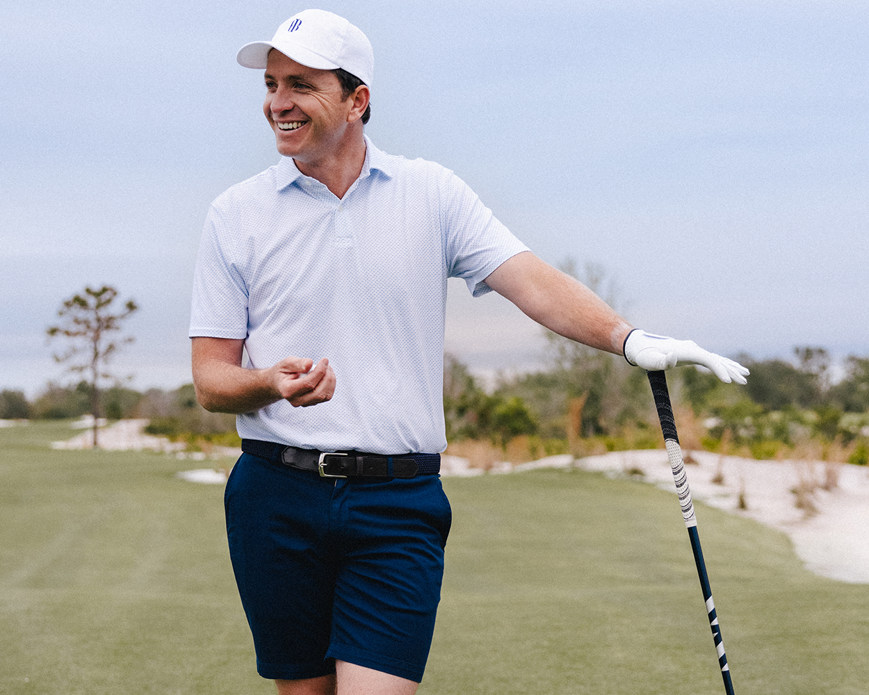 Man on golf course wearing The Cameron Short: Navy, leaning on a golf club, showcasing comfort and style with garment-washed cotton/stretch twill fabric.