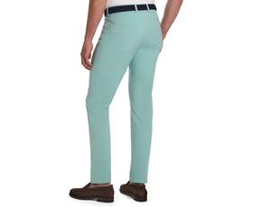 Rear view of a man wearing The McDaniel 5 Pocket Pant: Cascade Green, showcasing slim-fit trousers with a woven belt and brown suede loafers.
